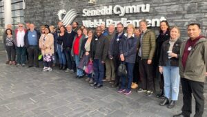Grŵp o bobl yn sefyll y tu allan i Senedd Cymru || Group of people standing outside Welsh Parliament