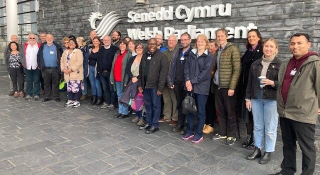 Grŵp o bobl yn sefyll y tu allan i Senedd Cymru || Group of people standing outside Welsh Parliament